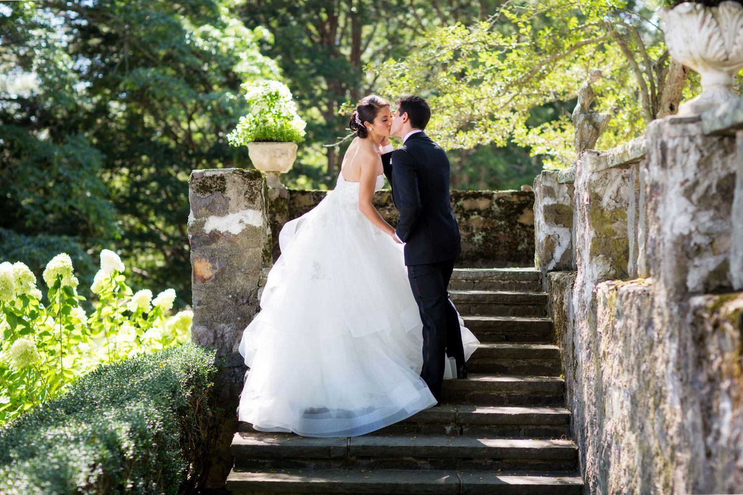 A romantic wedding couple shares intimate moments on rustic stone steps surrounded by lush greenery.