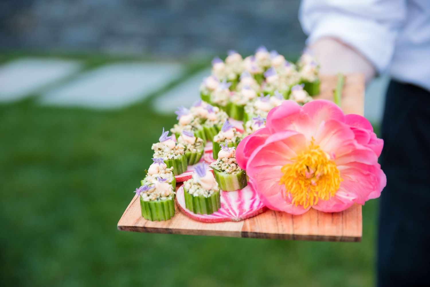 Wooden serving tray with pink flower garnished appetizers and a large coral-colored bloom.
