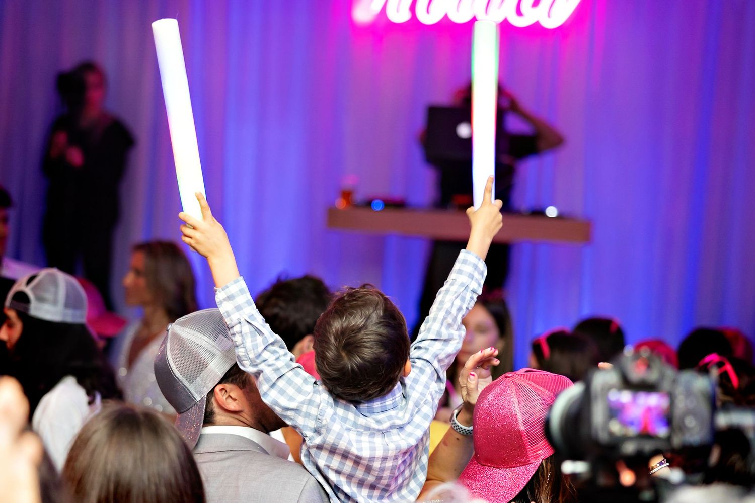 Party guests holding glowing light sticks in the air at a festive event with purple lighting.