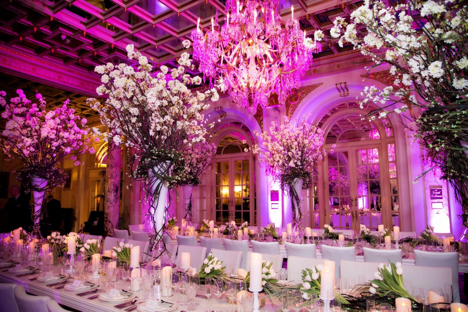 Elegant ballroom decorated with pink lighting, crystal chandeliers and cherry blossom trees.