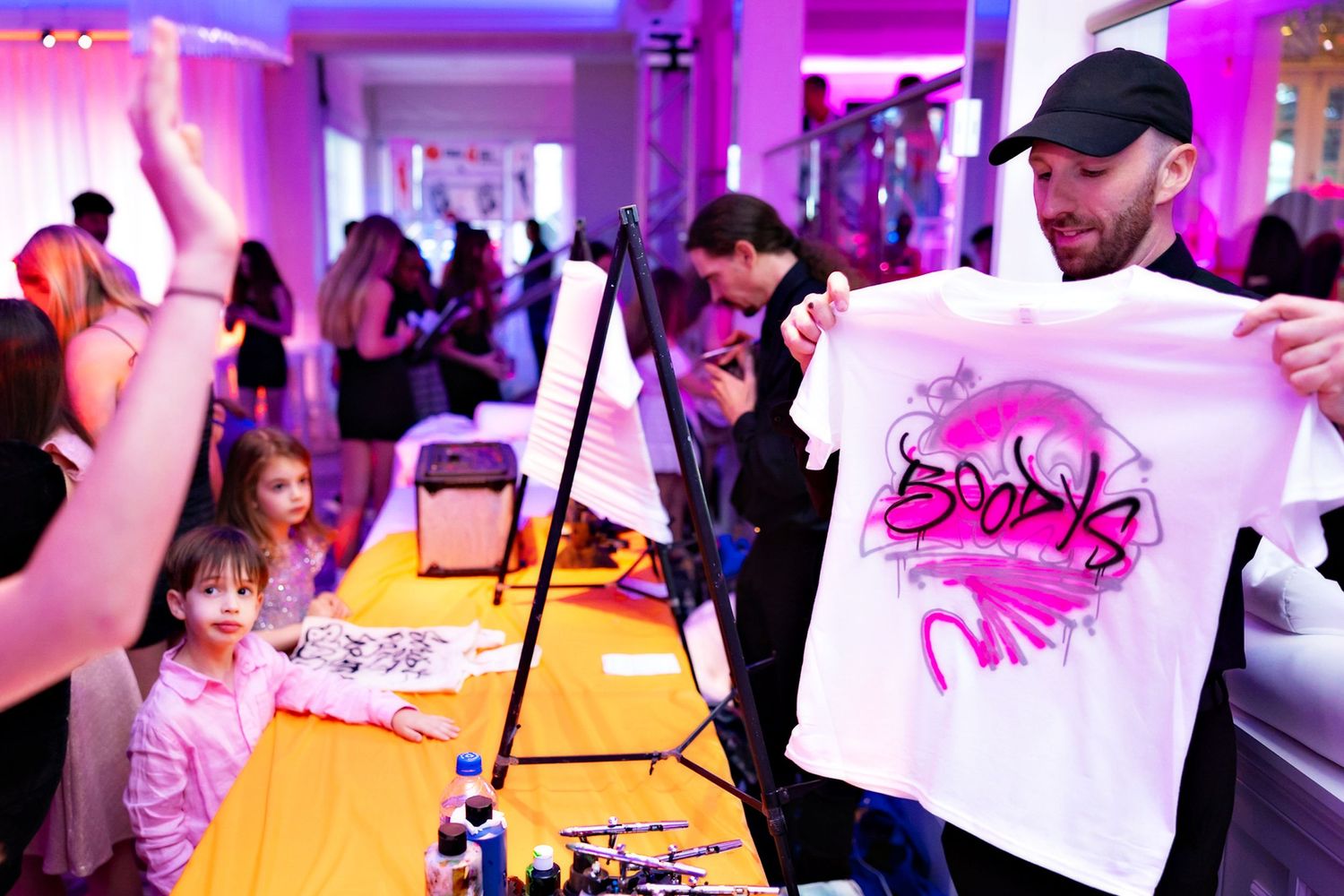 Custom t-shirt station at an event with pink lighting and display setup.