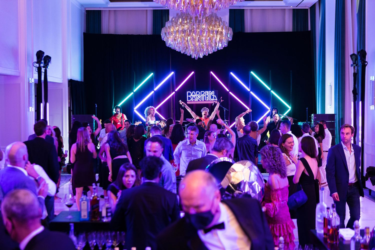 Crowded formal event with neon lighting and chandelier in an elegant ballroom setting.