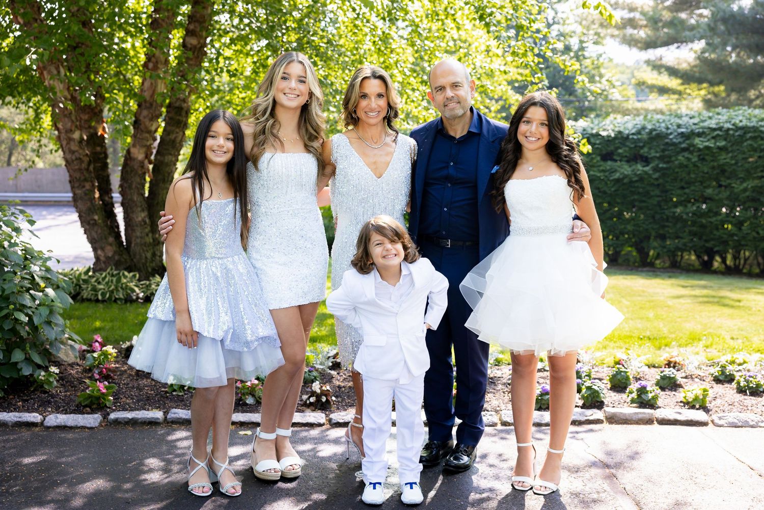 A group poses together outdoors wearing coordinating white and light colored formal attire.