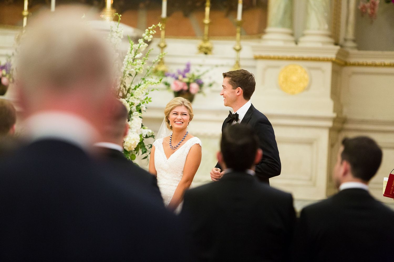 A couple shares a joyful moment during their wedding ceremony in an elegant indoor venue with chandelier lighting.