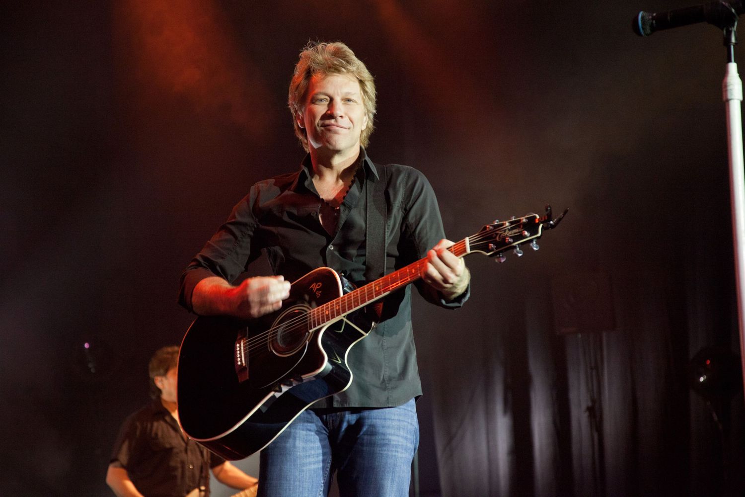 A musician performs on stage with an acoustic guitar under dramatic red lighting.