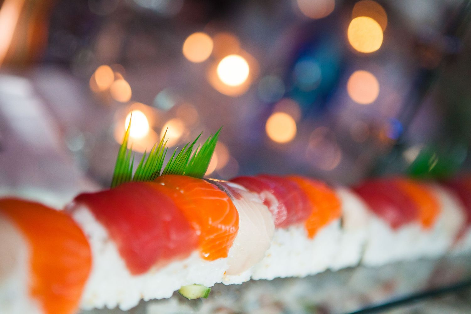 Close-up of colorful sushi nigiri pieces arranged in a line with bokeh background.