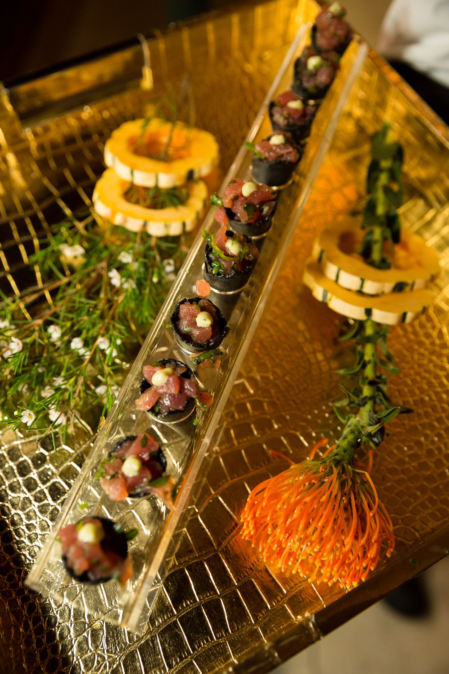 Elegant appetizers artfully arranged on a long glass platter with decorative herbs and garnishes on a golden surface.