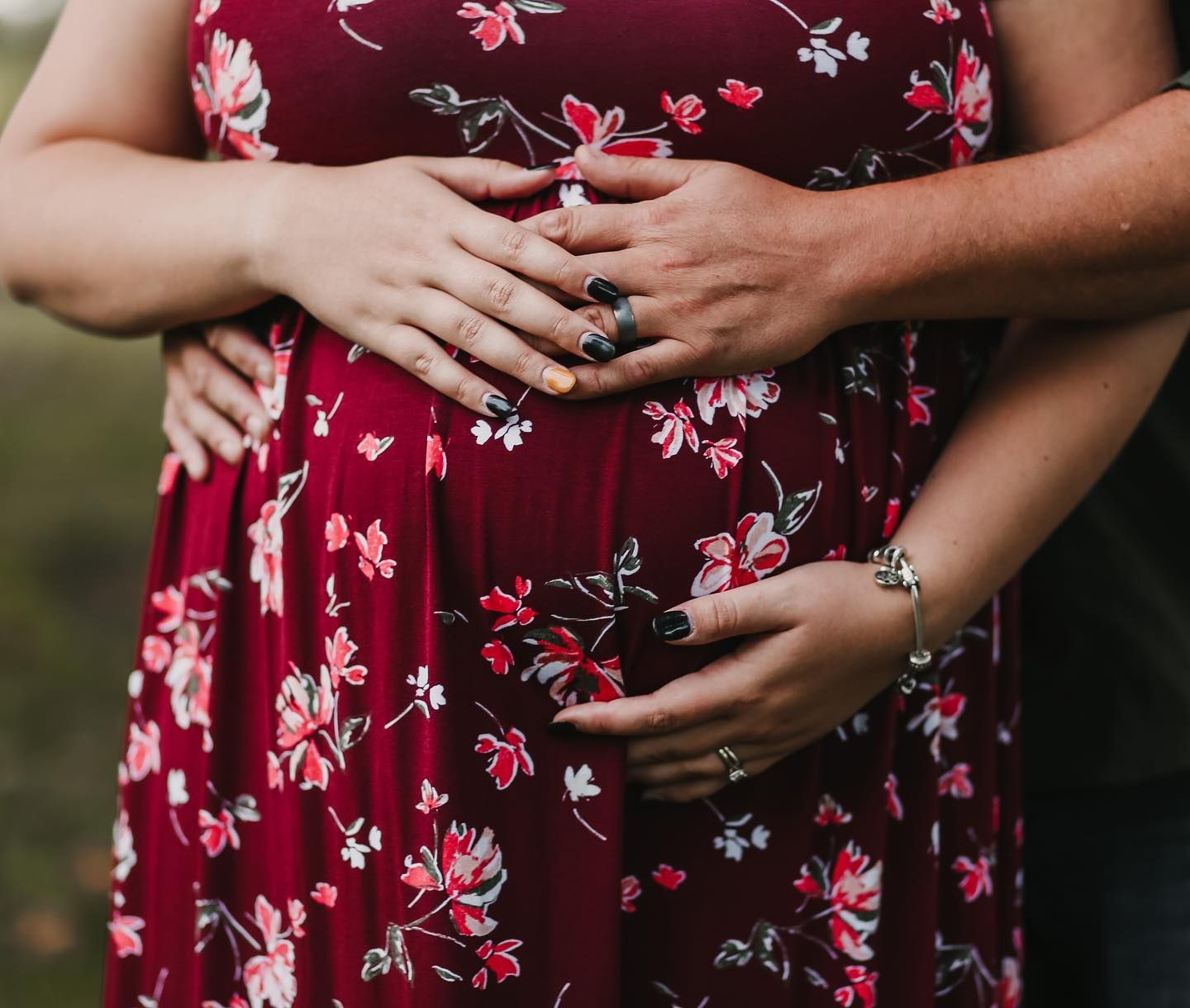 Close-up of hands resting on a floral burgundy dress showing rings and tender embrace.