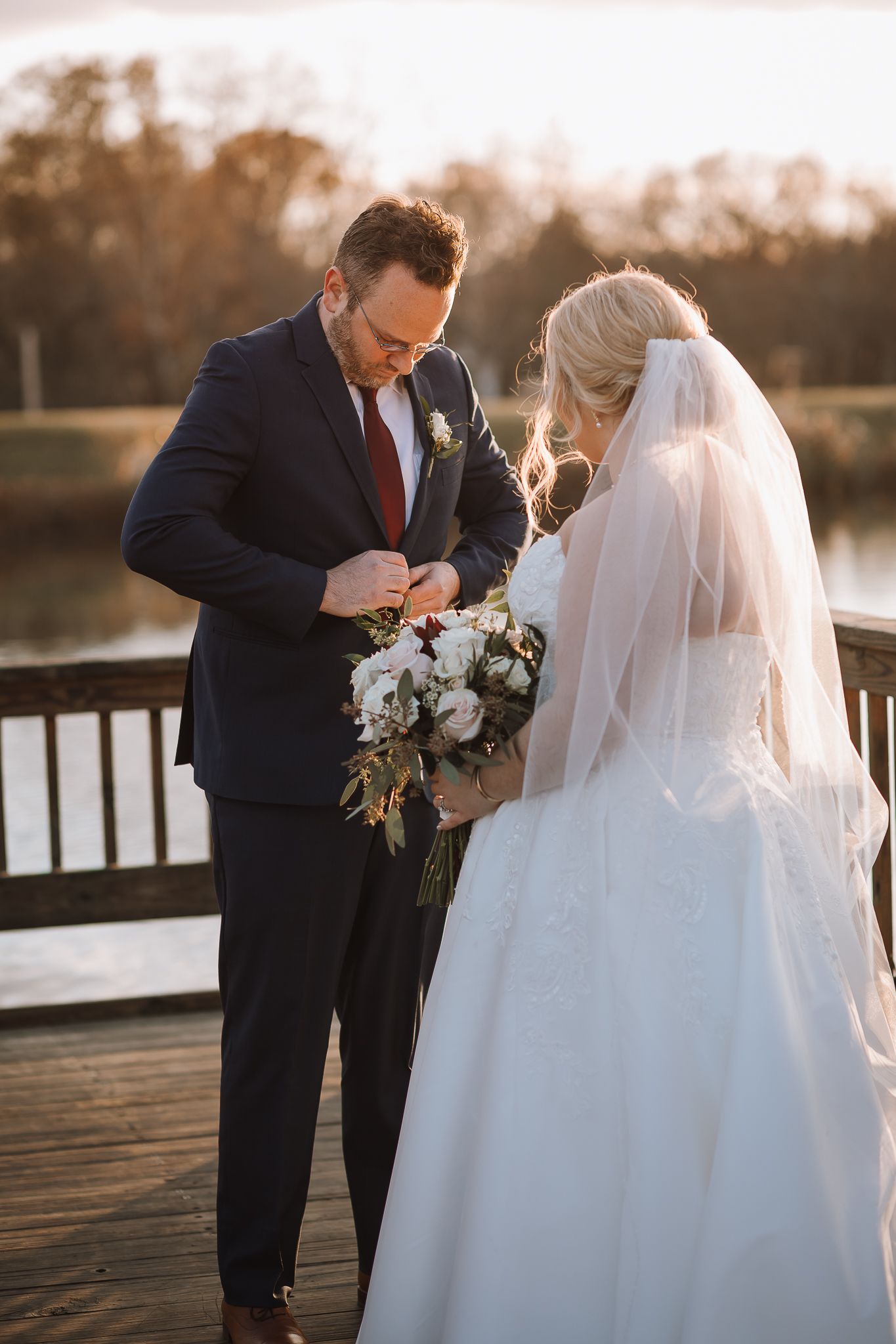 Wedding couple sharing intimate moment on wooden dock during golden hour sunset.