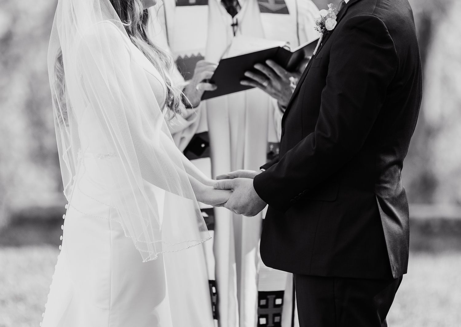 Black and white photo of couple holding hands during outdoor wedding ceremony.