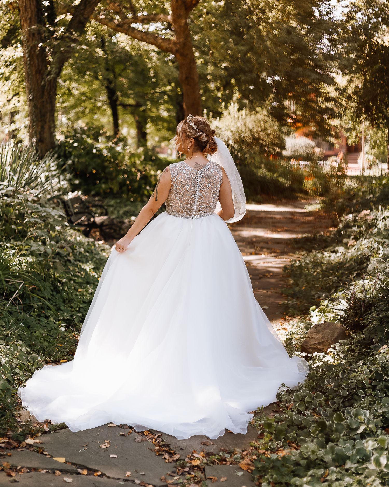 Back view of bride in lace-detailed ballgown walking through garden path.