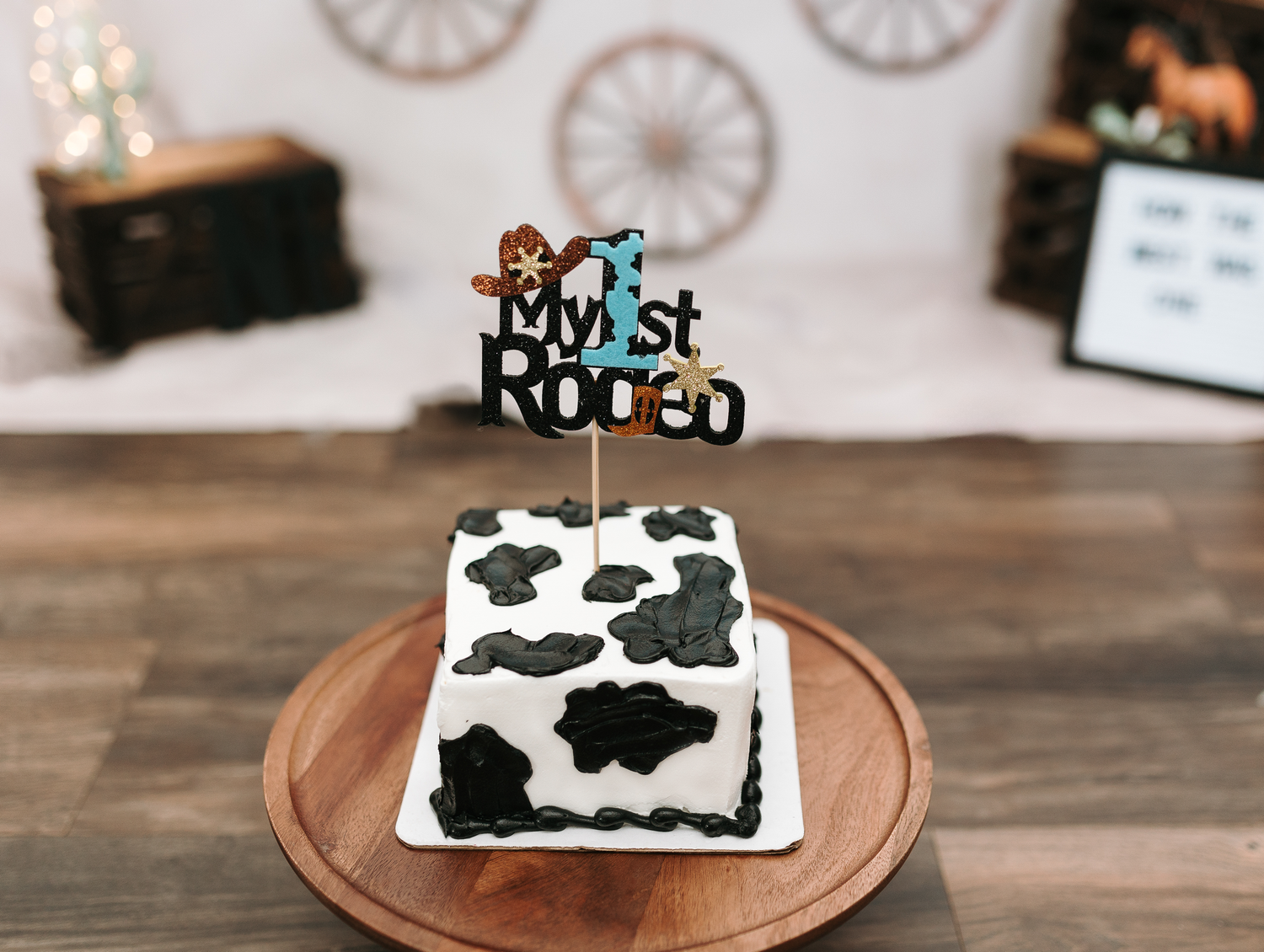 Cow print smash cake with 'My First Rodeo' topper on wooden platter.