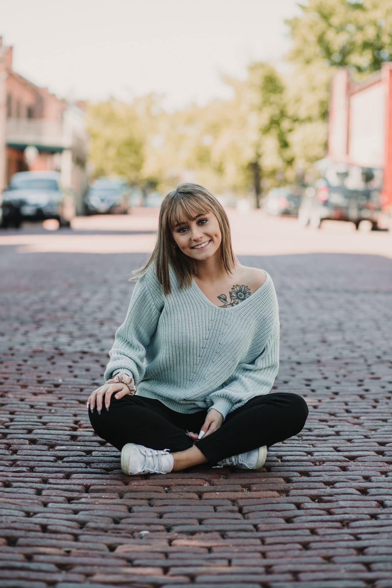 Casual portrait sitting on brick street in mint sweater with visible tattoo.