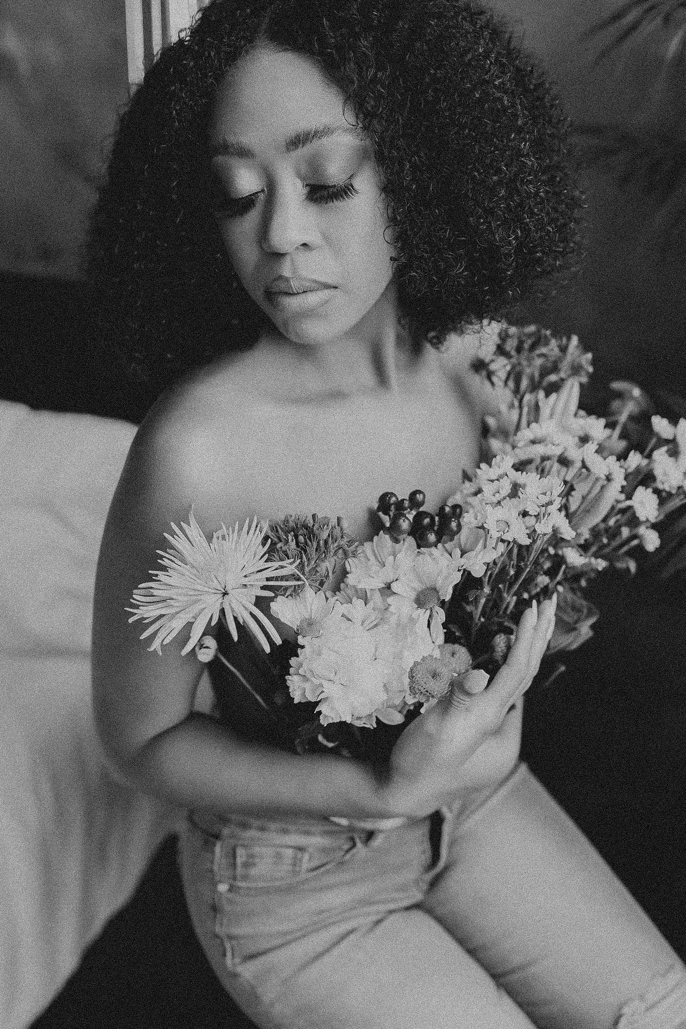 Black and white portrait of person with curly hair holding mixed flower bouquet against light background.