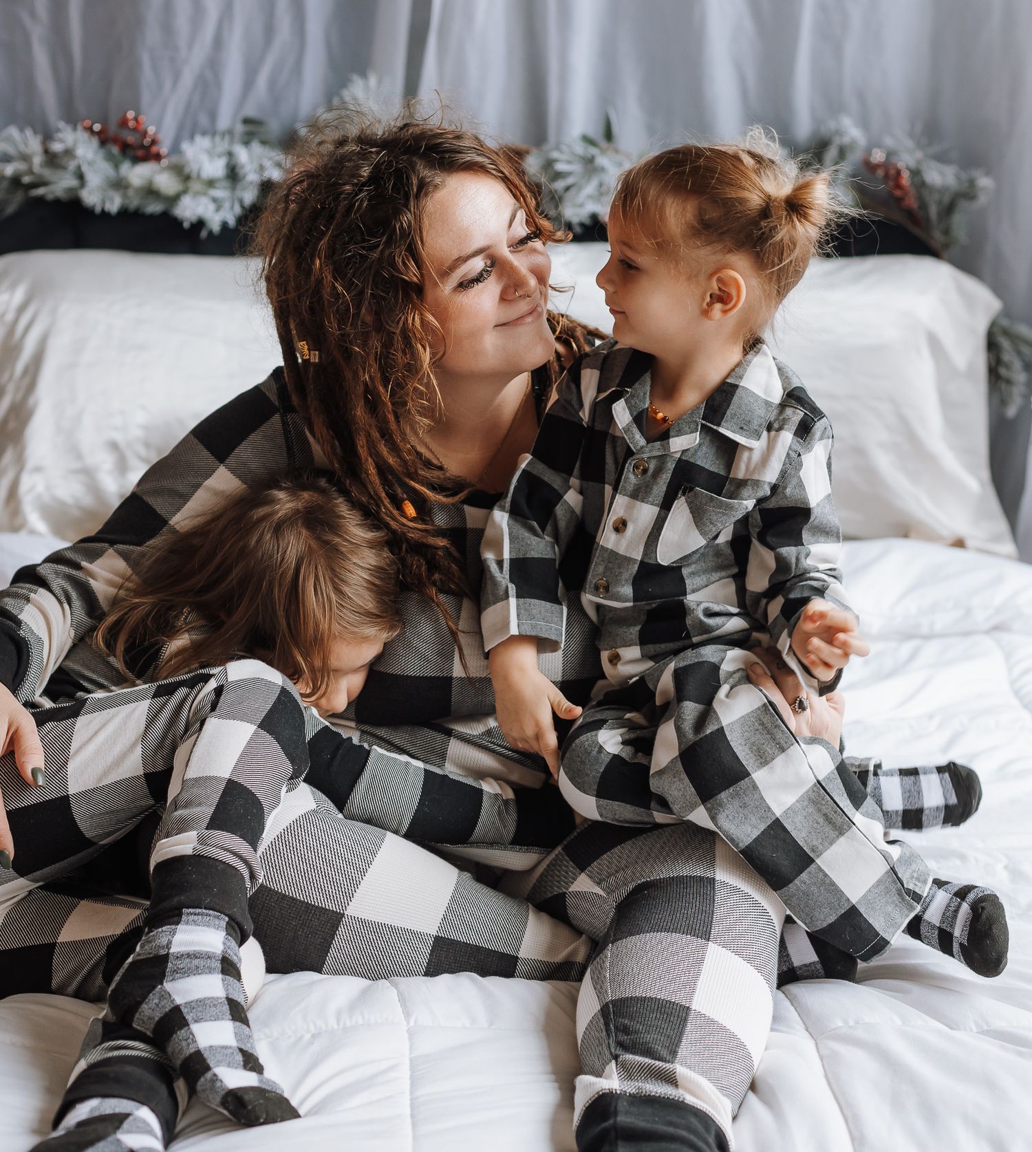 A cozy family moment in matching buffalo plaid pajamas on a white bed.