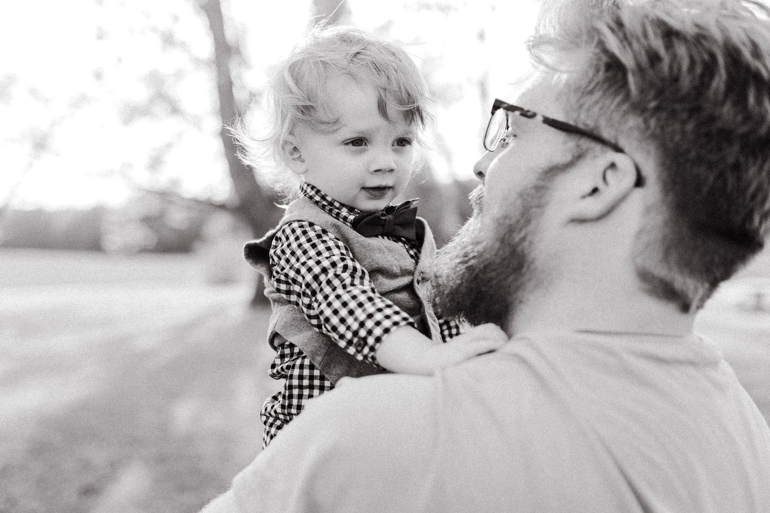 Black and white portrait of a tender parental moment in natural outdoor setting.