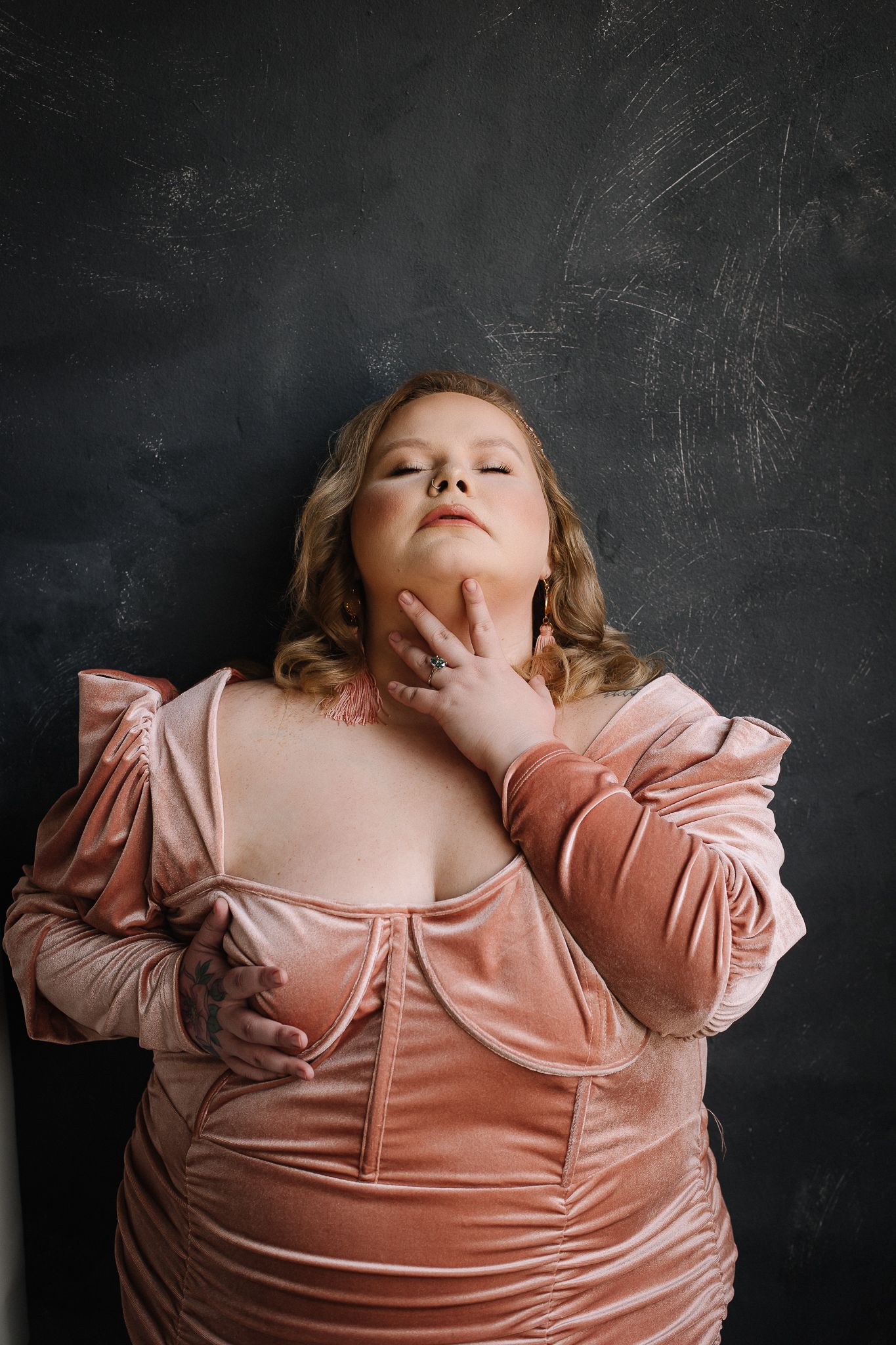 Portrait against chalkboard backdrop wearing pink satin top with dramatic pose.