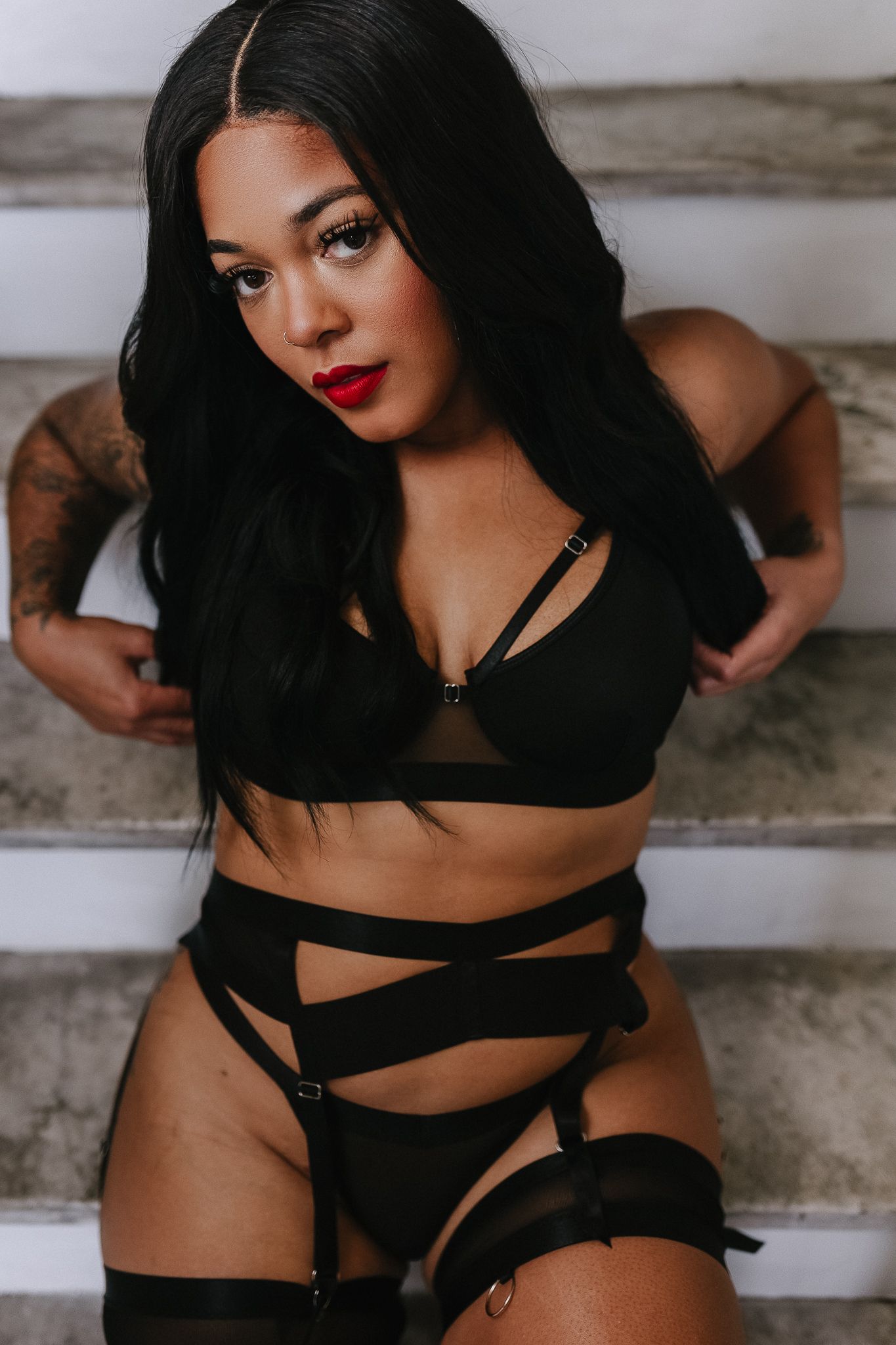 Dramatic portrait in black strappy lingerie against neutral backdrop.