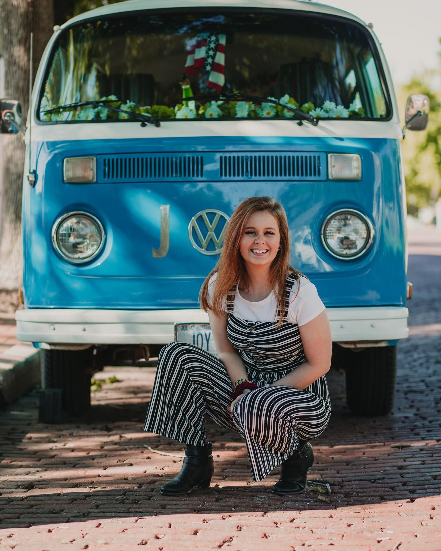 Portrait in front of bright blue vintage VW bus wearing striped jumpsuit.