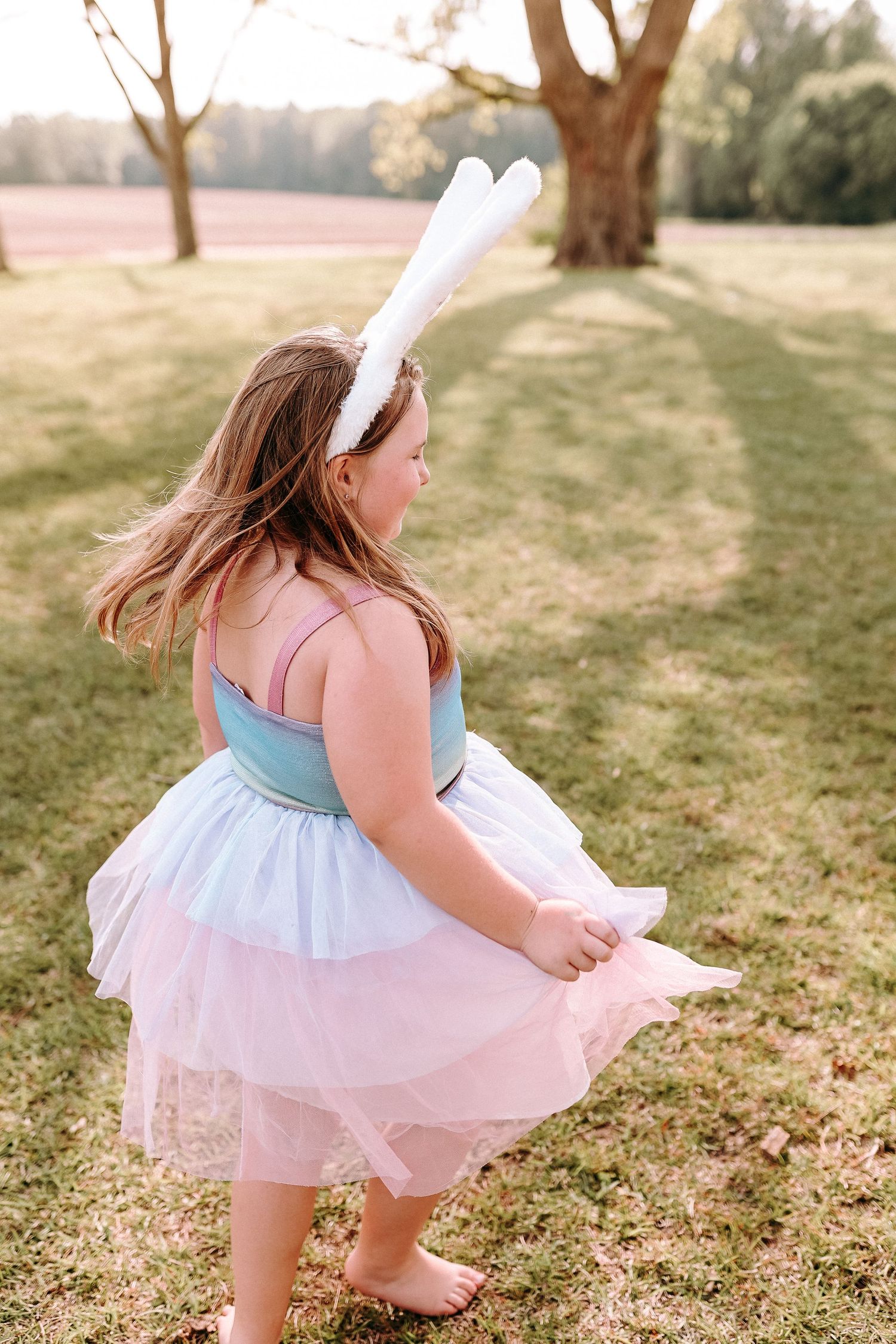 A ethereal spring scene with a tulle dress and bunny ears headband in a sunlit garden meadow.