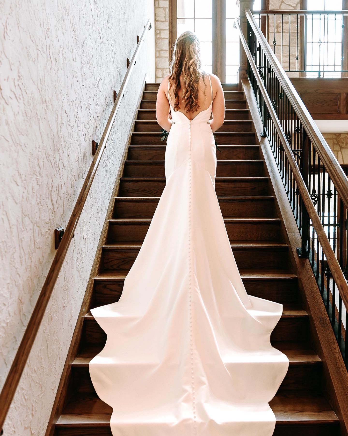 Bride in flowing white gown ascending elegant staircase.