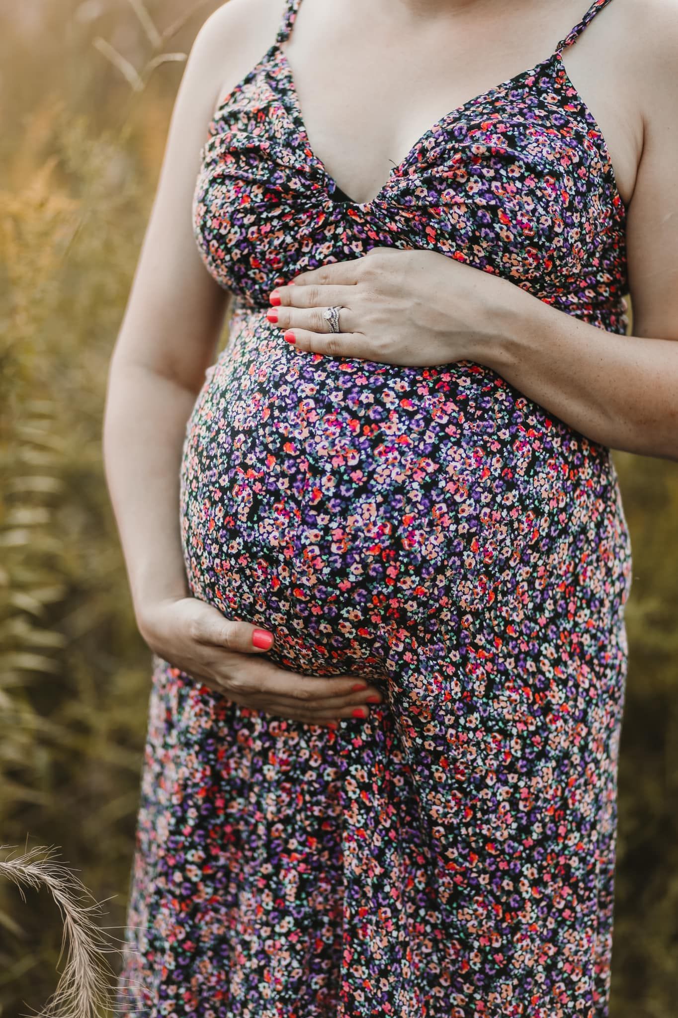 A pregnant belly in a floral dress captured against golden grass at sunset.