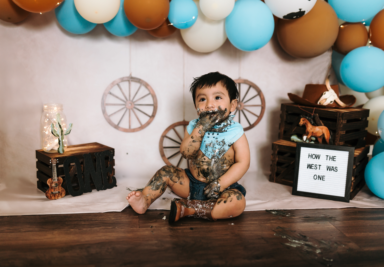 Western-themed birthday setup with blue and brown balloons featuring a small child in cowboy attire.