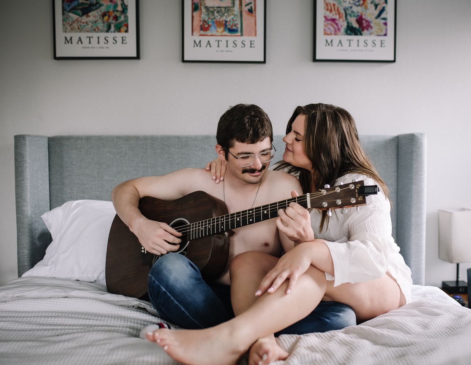 Intimate lifestyle portrait of couple sitting on bed with acoustic guitar.