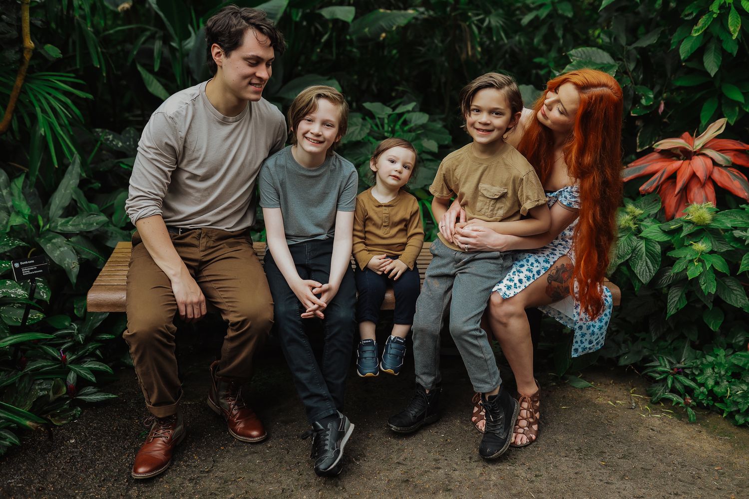A candid family photo on a bench surrounded by tropical plants in a greenhouse setting.