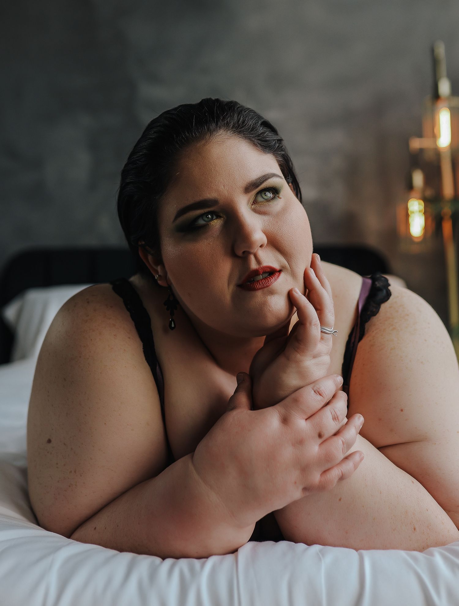 Intimate boudoir portrait against dark backdrop featuring soft lighting and white bedding.