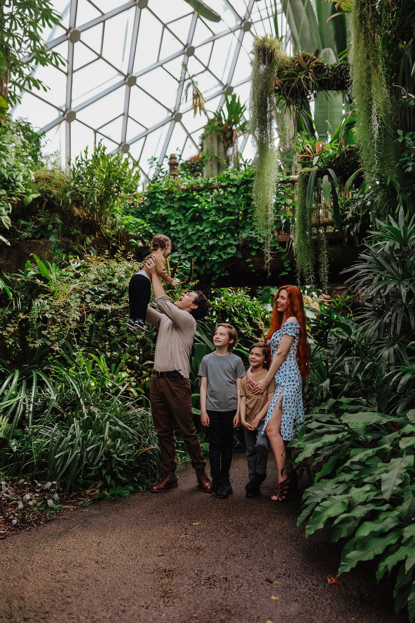Family gathering in botanical garden with glass dome ceiling and hanging plants.