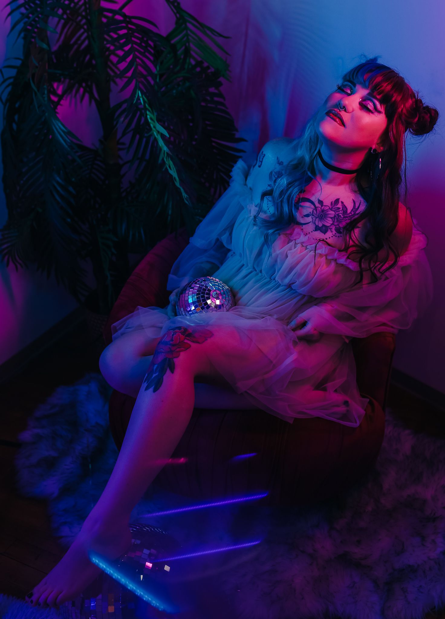 Atmospheric boudoir portrait with neon lighting and disco ball against tropical foliage.