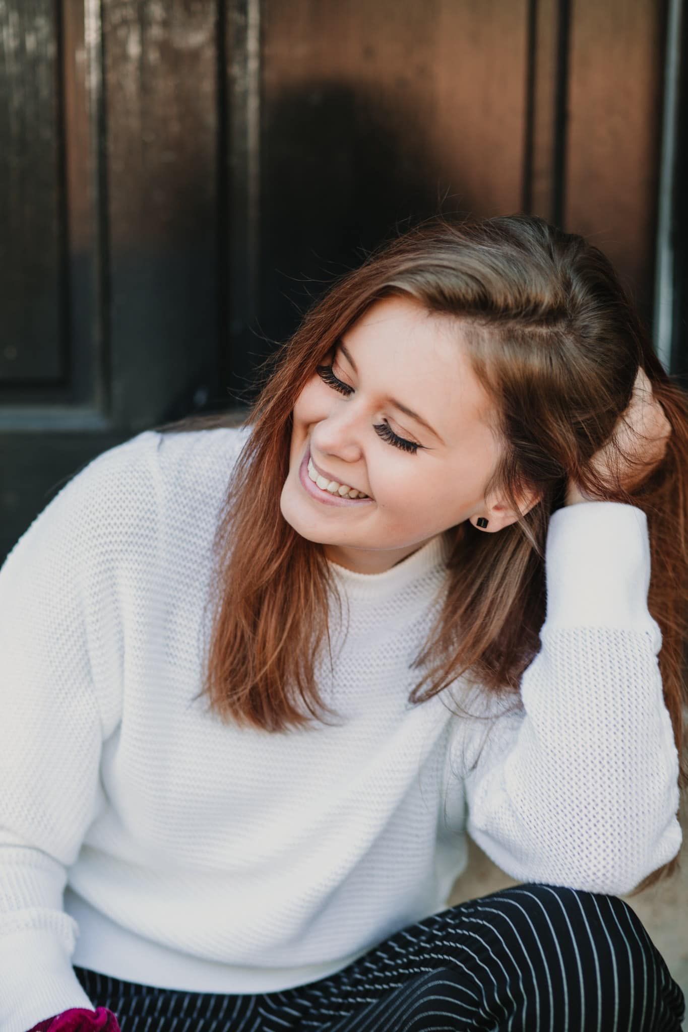Casual portrait of person in white sweater laughing with eyes closed.