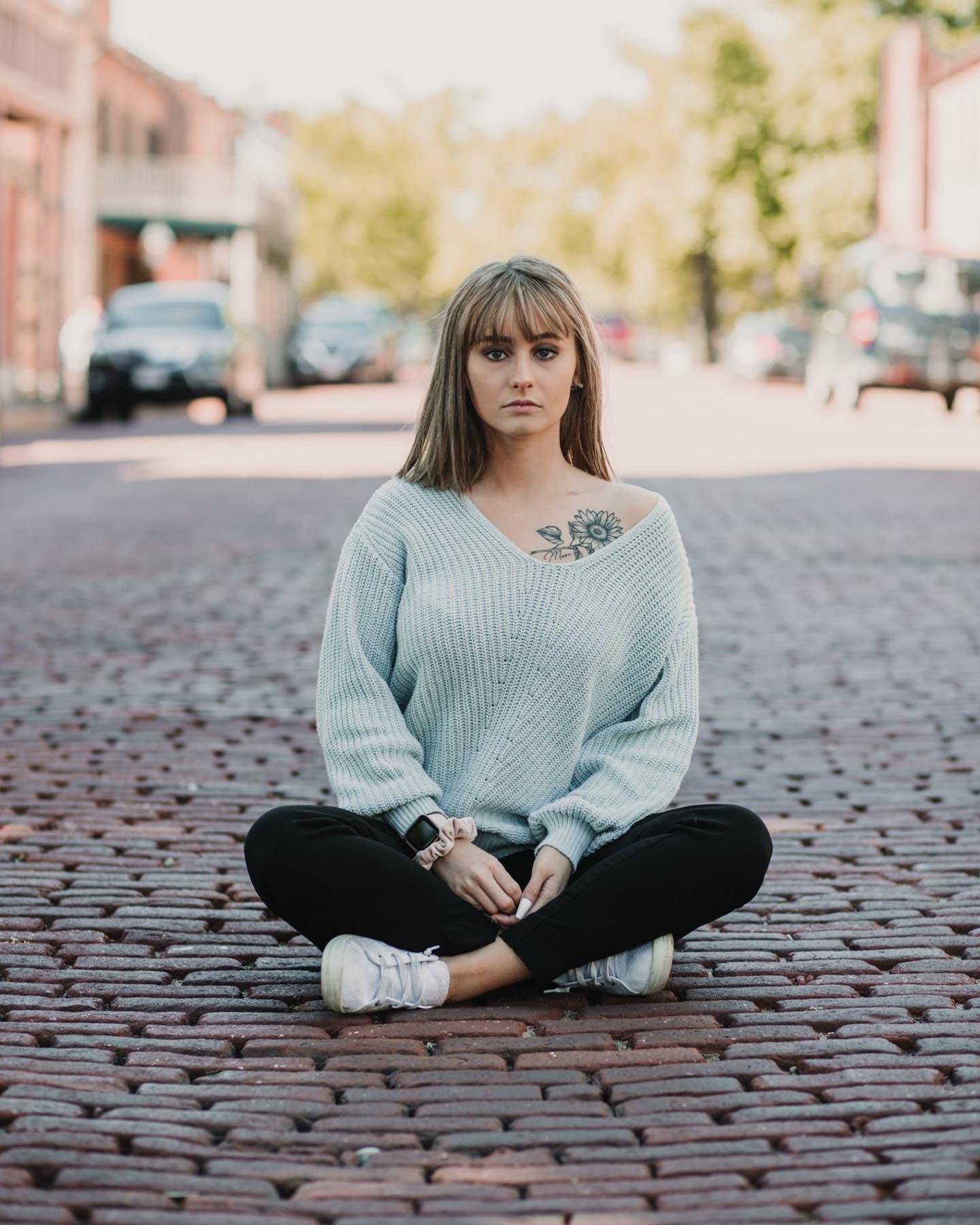 Street style portrait on cobblestone street in light blue sweater and white sneakers.