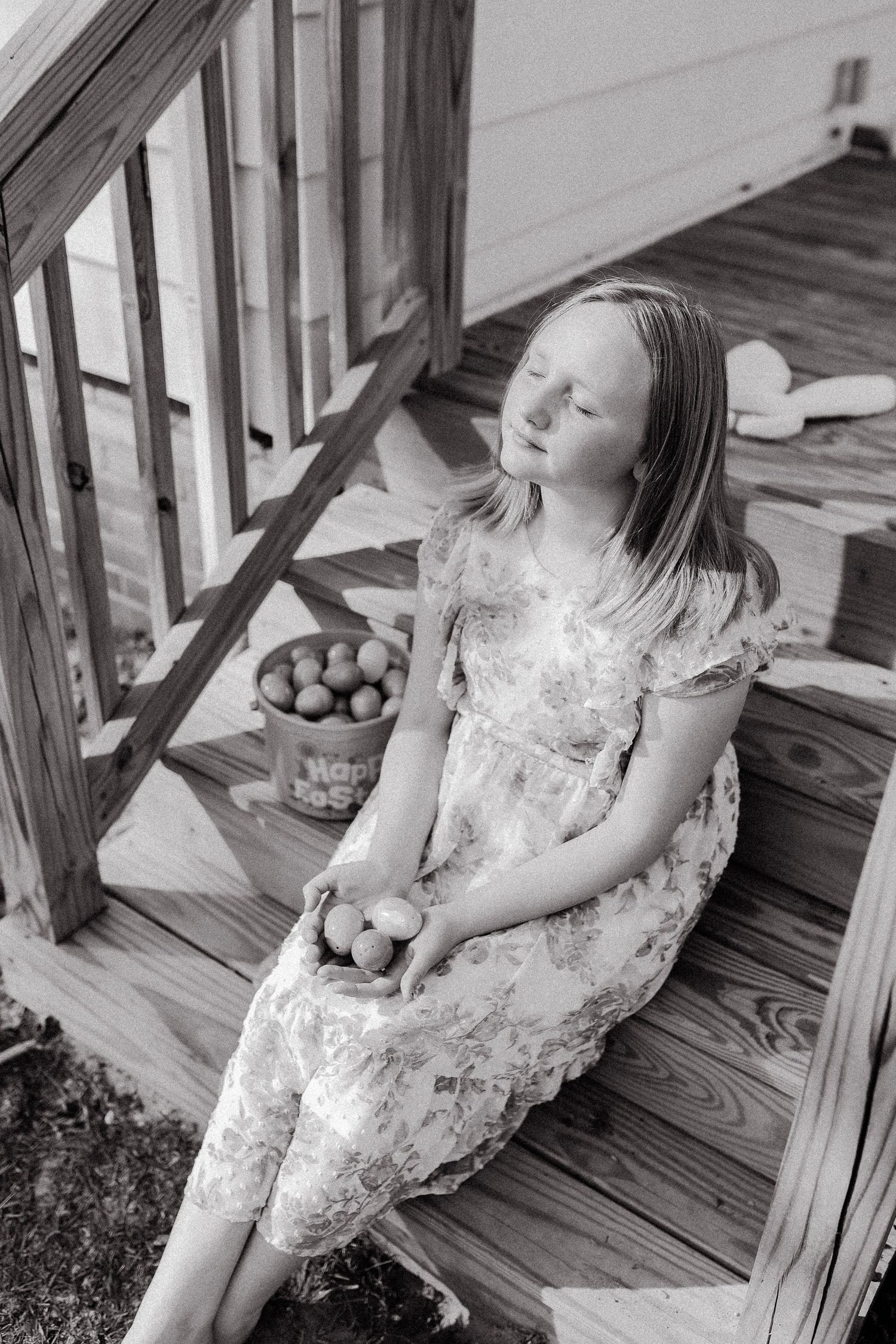 A black and white photo of someone sitting on wooden porch steps with fresh produce.