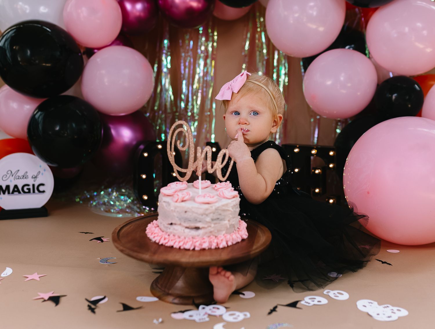 Birthday celebration with pink and black balloons surrounding a pink cake on a wooden table.