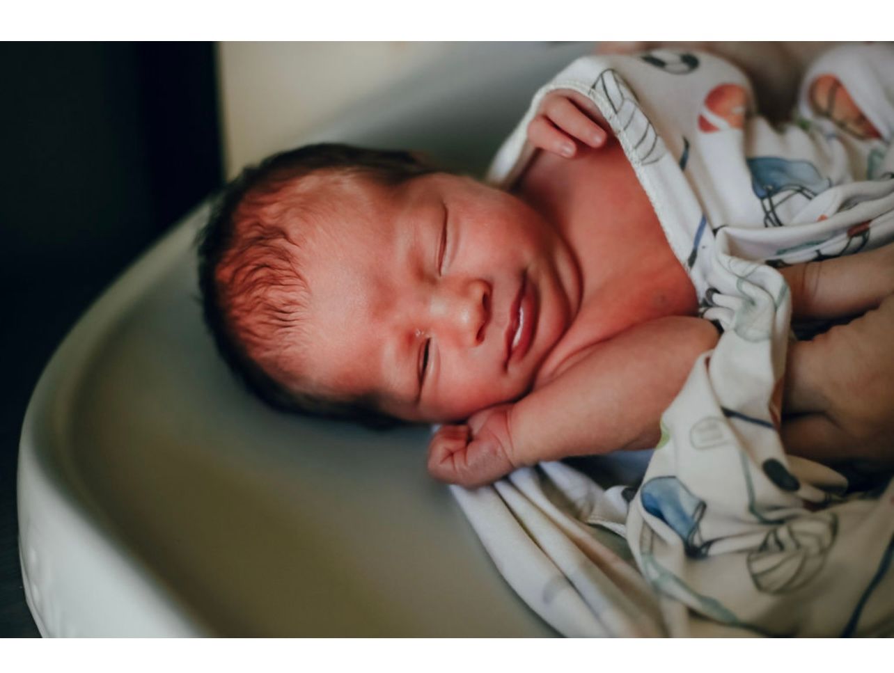 Peaceful newborn baby sleeping wrapped in a patterned blanket, resting in a hospital bassinet.