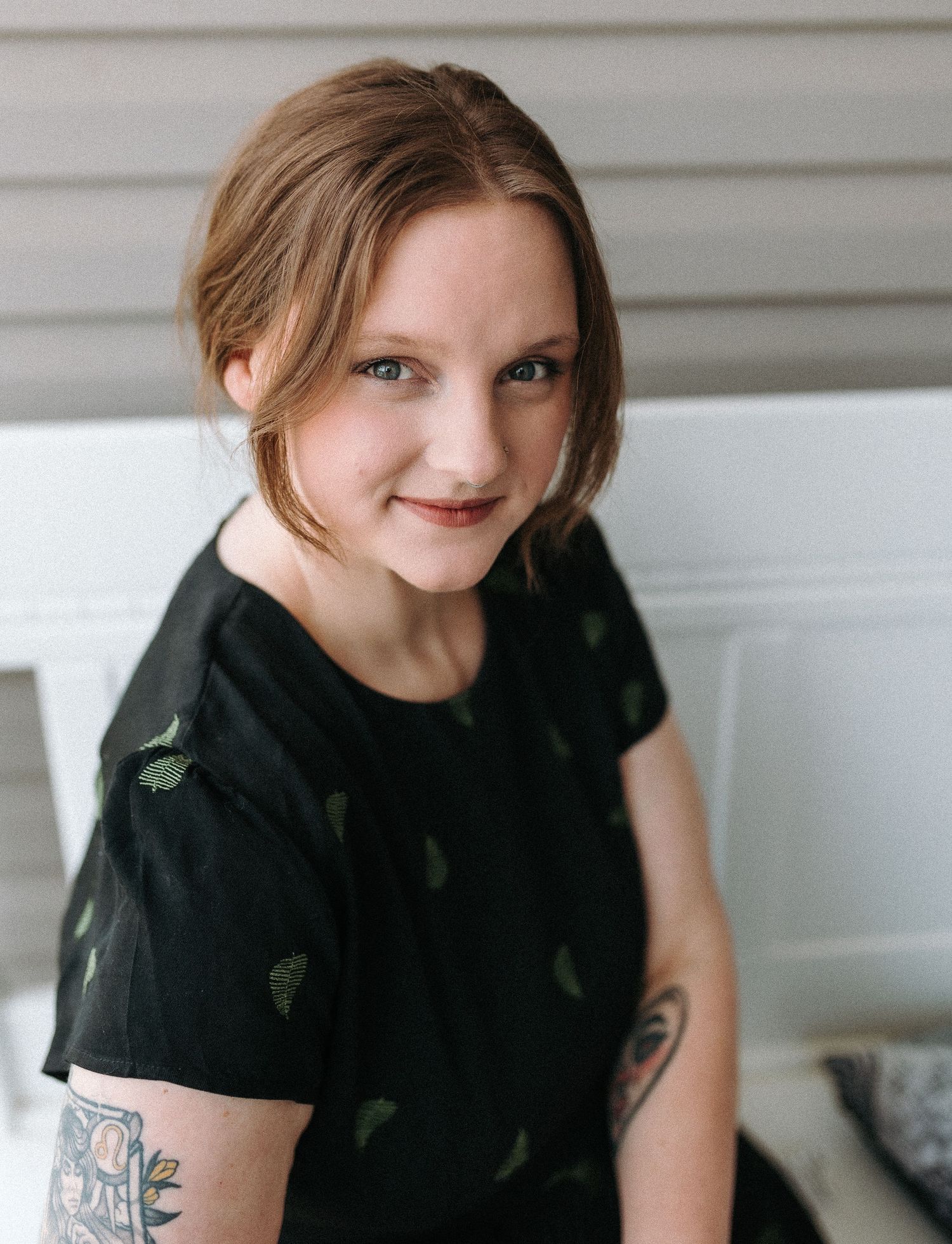 Portrait of a person in black t-shirt with tattoo against white wall.
