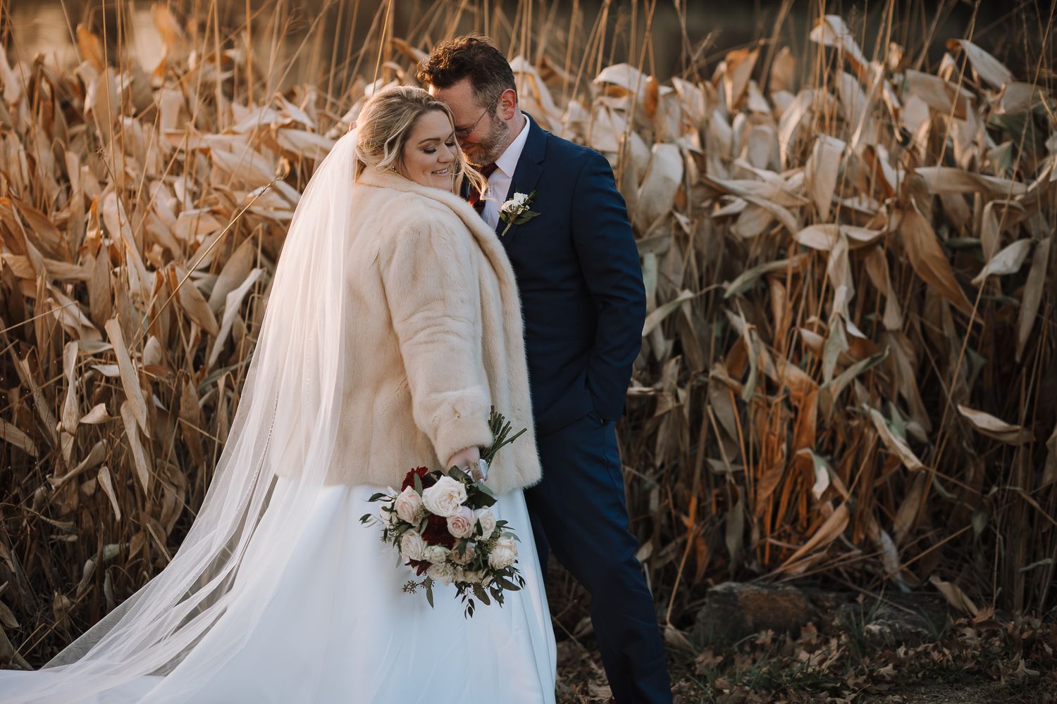 Wedding couple shares romantic moment in front of autumn corn field at sunset.