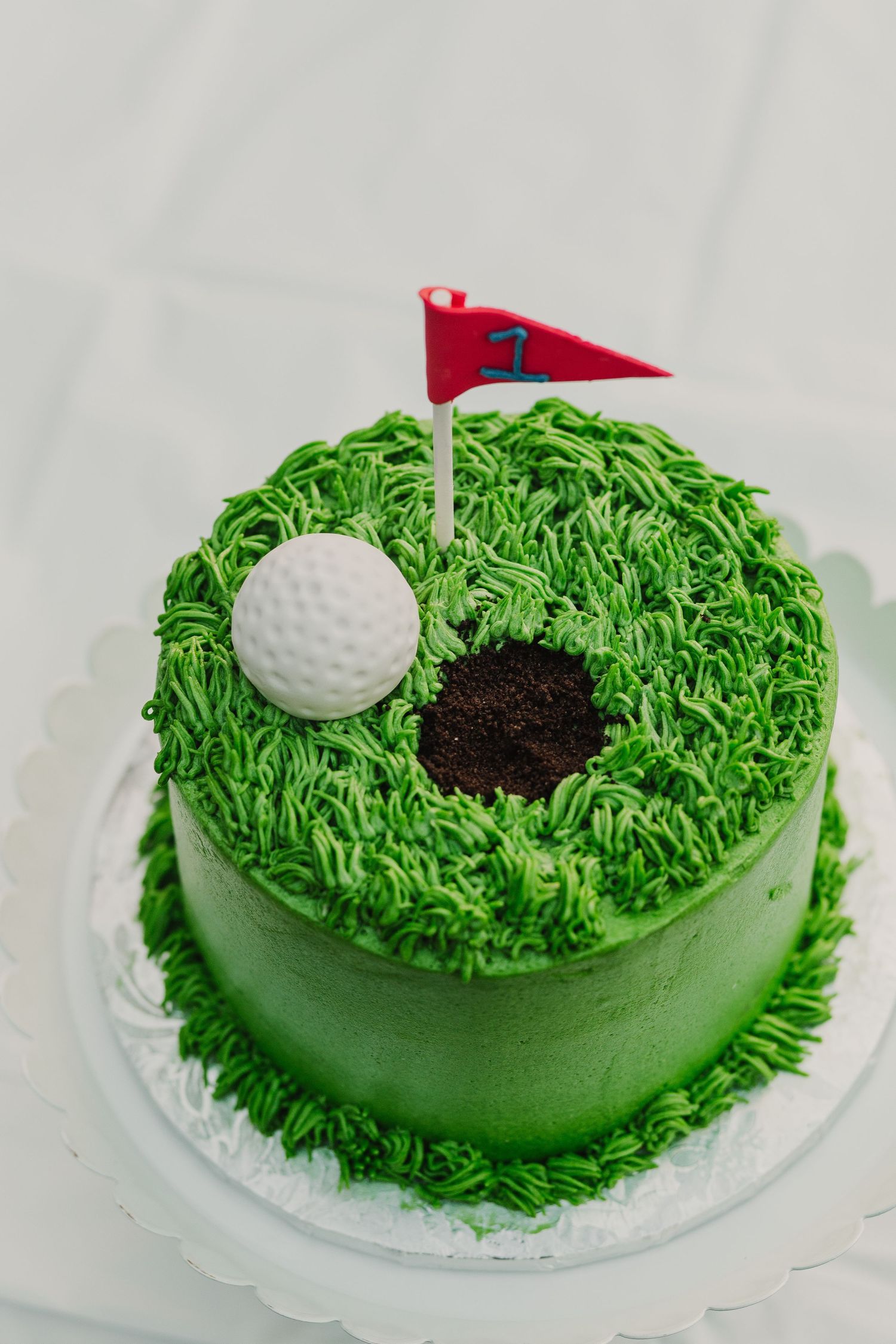 A golf-themed birthday cake with green frosting grass, white ball, and red flag decoration.