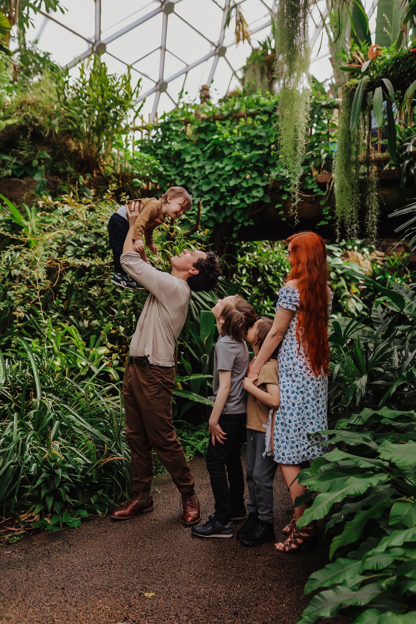 A heartwarming scene in a lush greenhouse with loved ones sharing a playful moment among tropical plants.