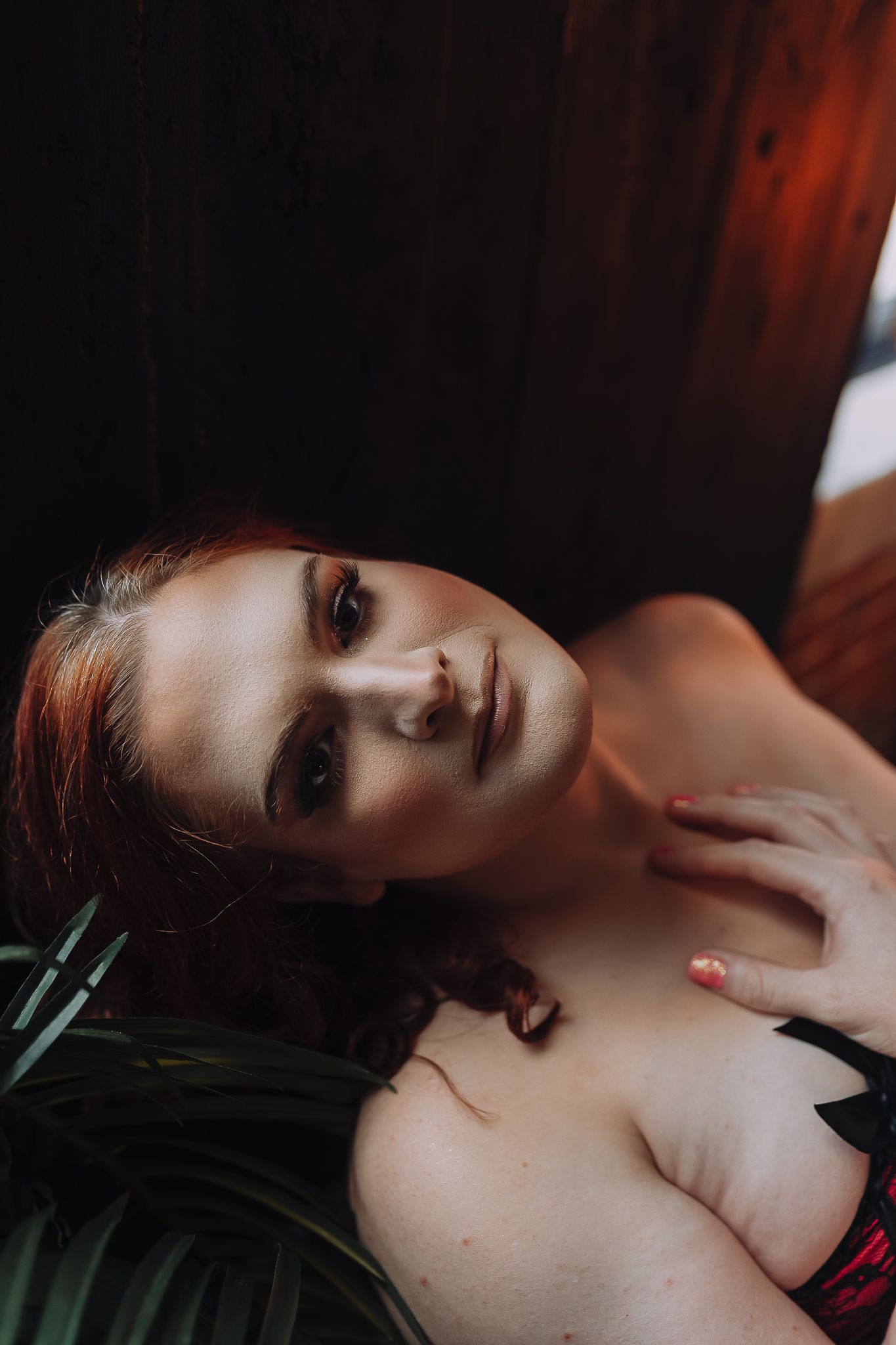 Artistic boudoir portrait in dark moody lighting with fern leaves and dramatic shadows.