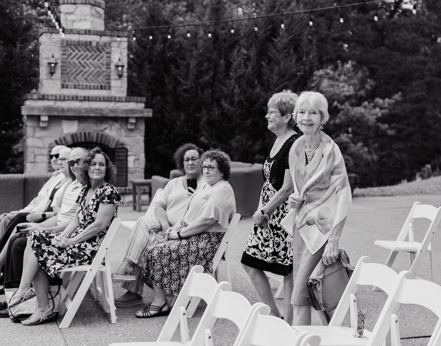 Vintage black and white photo of women seated on white chairs at an outdoor event.