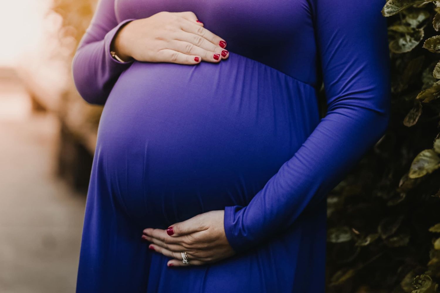 Close-up of hands cradling a pregnant belly in a royal blue maternity dress.