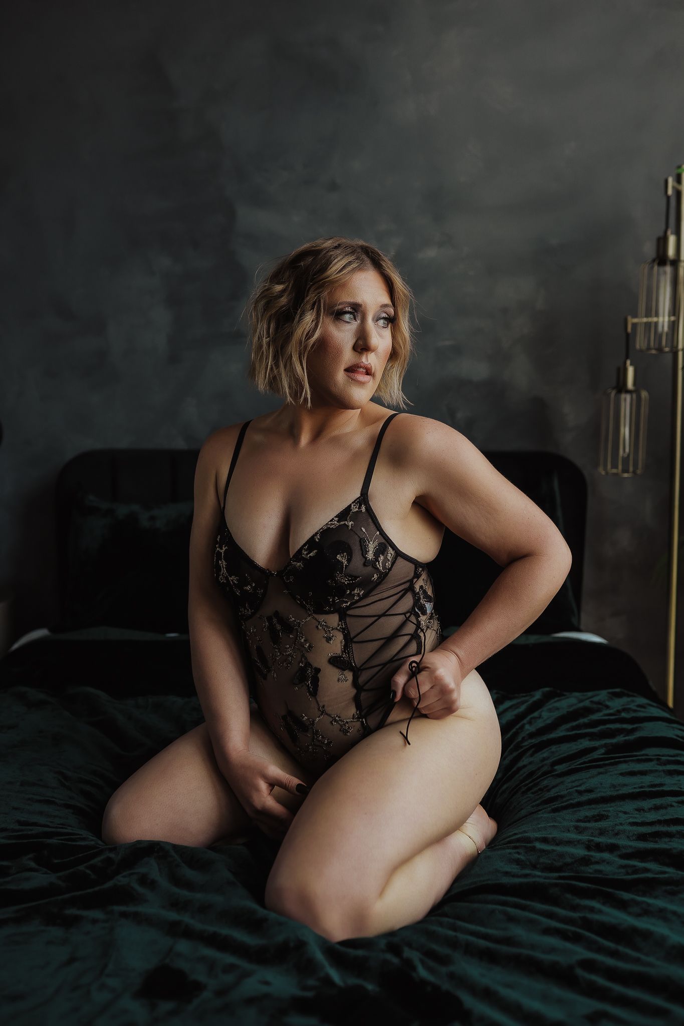A boudoir photoshoot features intimate styling against dark moody lighting and emerald green velvet bedding.