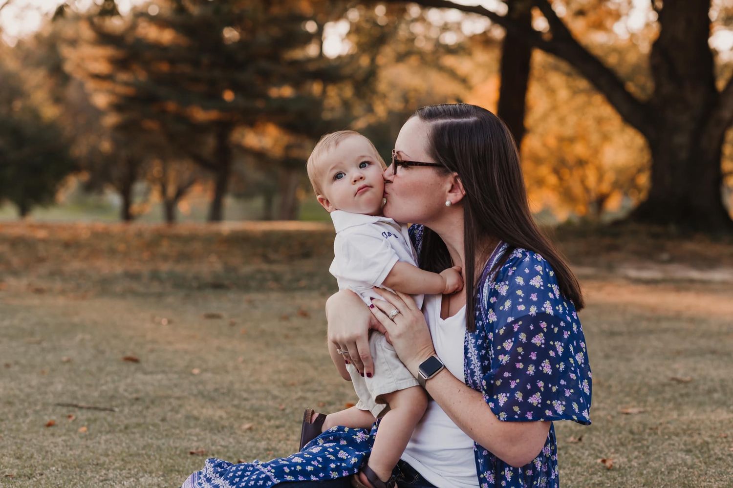 A tender moment shared outdoors during golden hour among autumn trees.