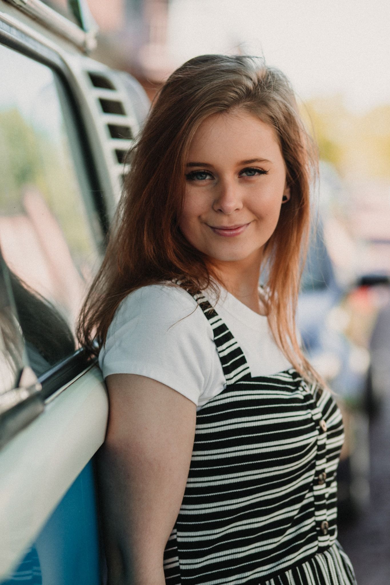 Retro-styled portrait next to classic car wearing striped overalls.