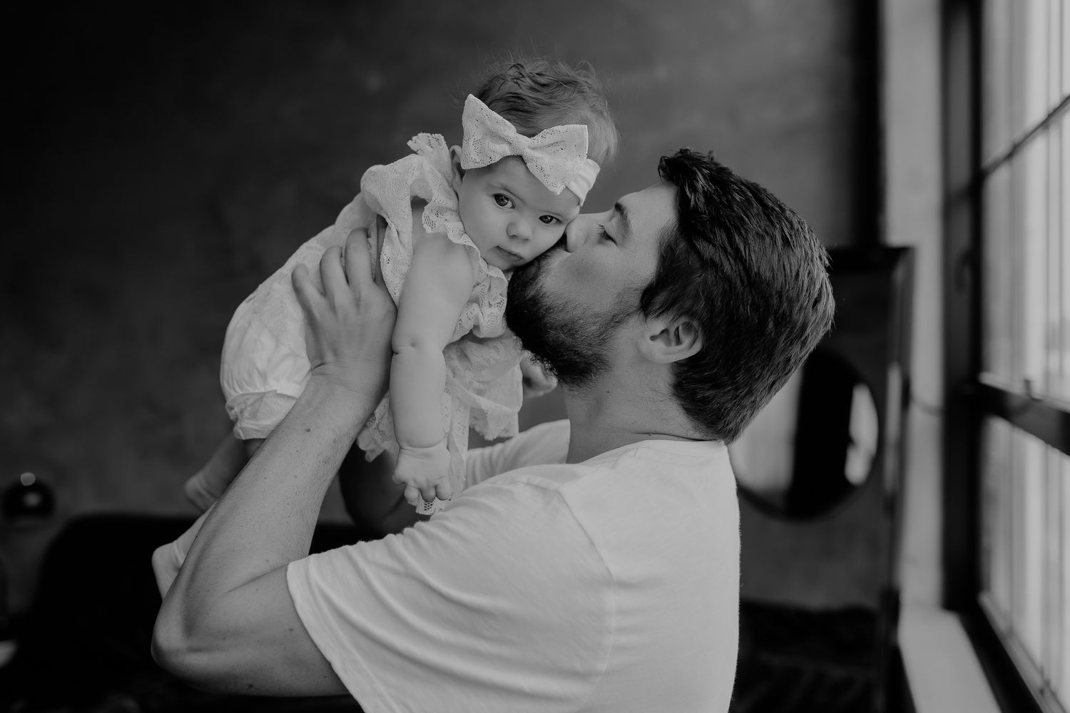 A tender black and white moment between parent and infant by a window.