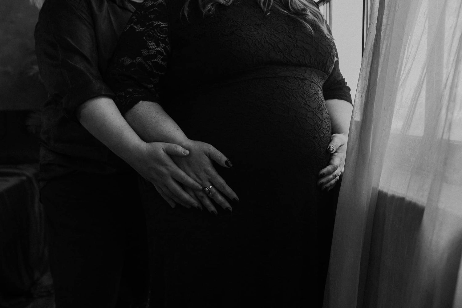 Silhouette of hands cradling a pregnant belly near a window.
