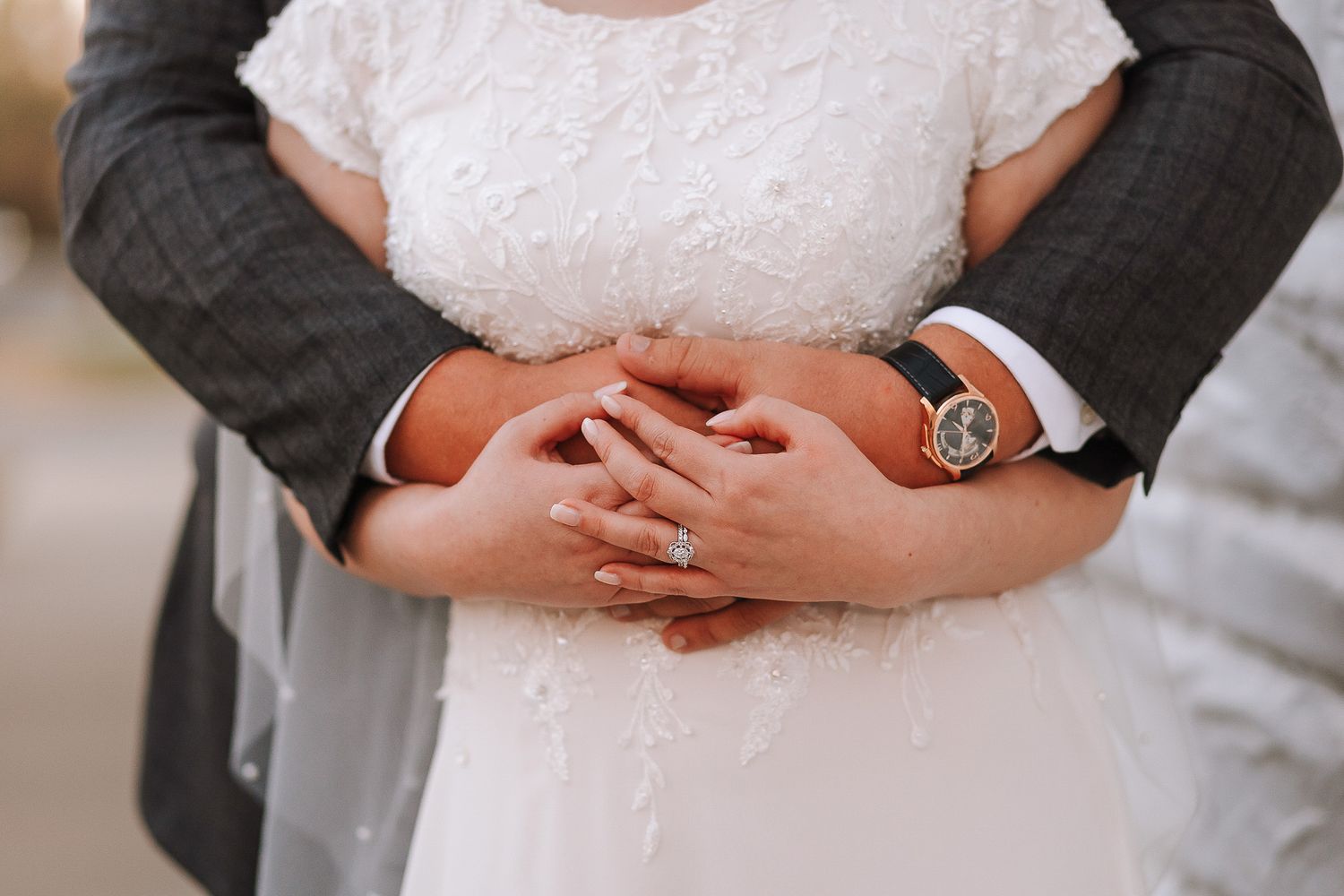 Close-up of couple's hands embracing during wedding ceremony showing rings and formal attire.